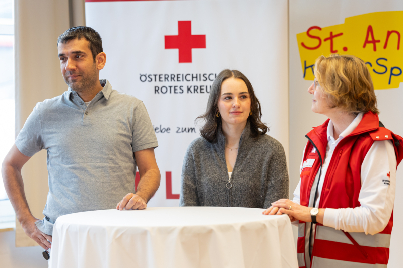Prof. Andische Andishe Attarbaschi, ehemalige Patientin Sarah Ellmer und Dr. Ursula Kreis vom Österreichischen Roten Kreuz vor einem weissen Stehtisch.