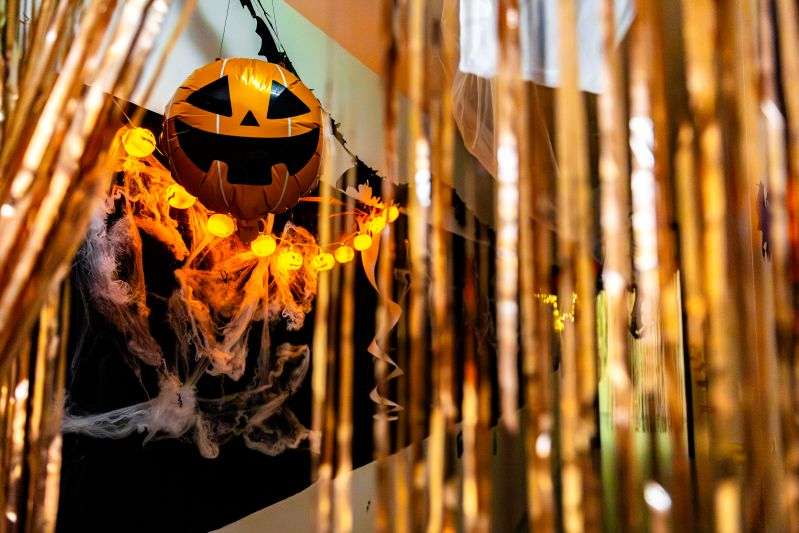 Halloween-Deko im Gang bestehend aus einem Kürbis-Luftballon, Lichterkette und goldenem Streifenvorhang.