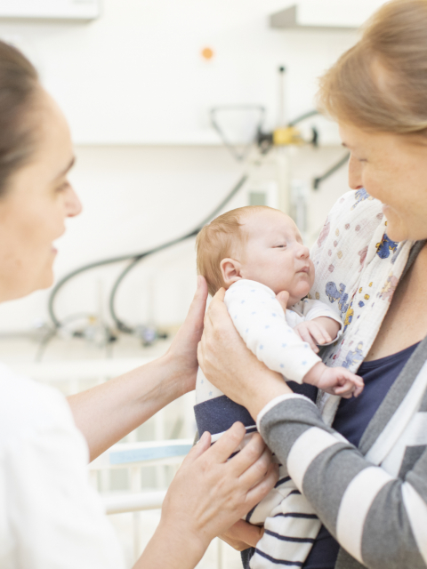 Mutter hält Baby im Arm und Ärztin steht daneben.